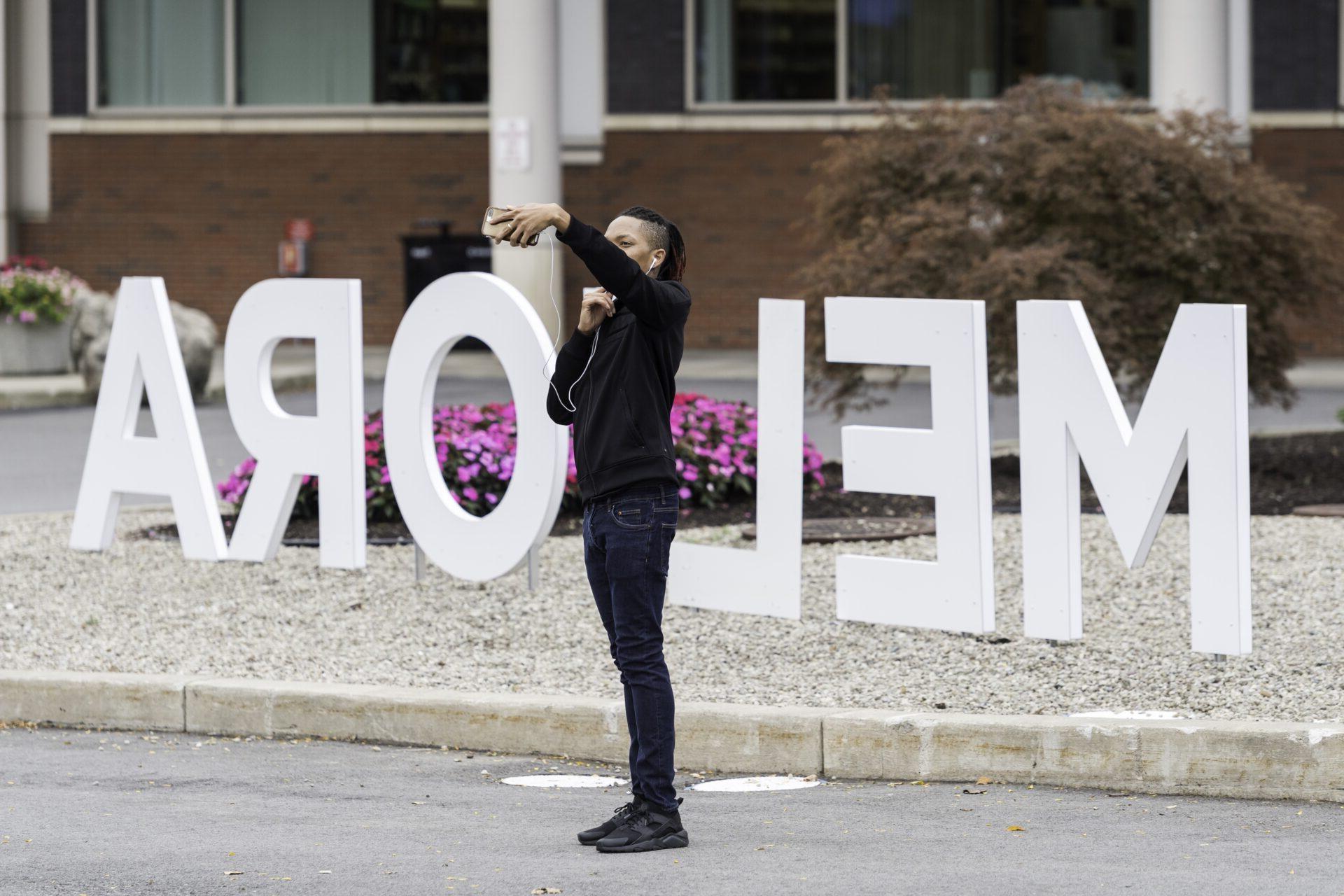 A student taking a selfie with the giant "Meliora" letters